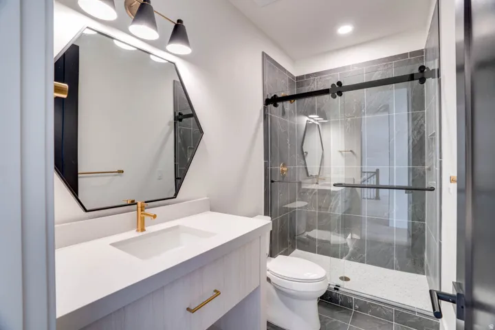 Contemporary bathroom featuring a white vanity with integrated sink, gold-finish faucet, and an octagonal mirror