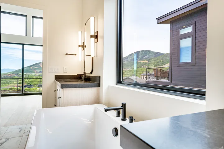 Freestanding soaking tub with a wall-mounted faucet, complemented by a vanity featuring a dark countertop, integrated sink, and contemporary lighting fixtures