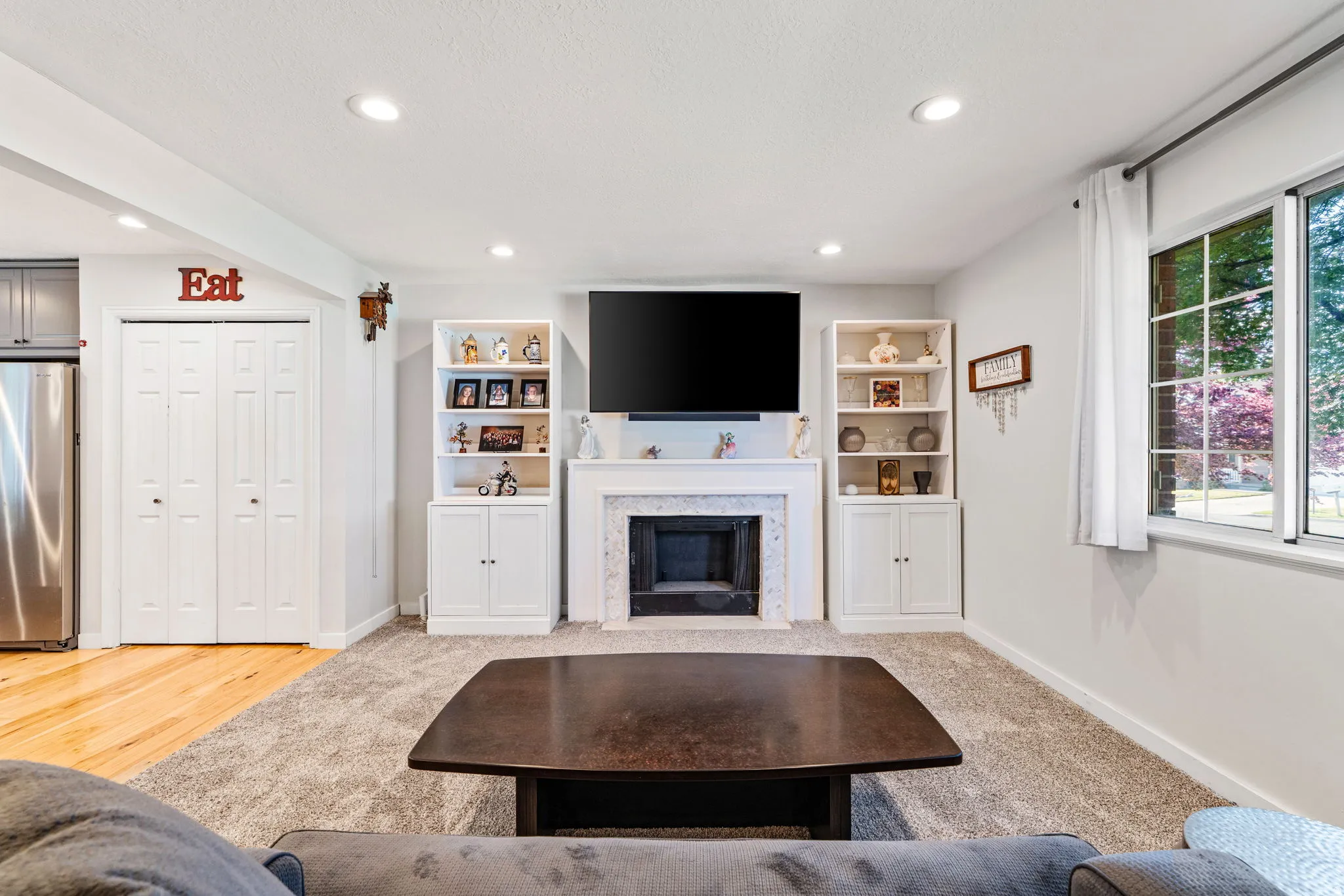 Living area featuring a fireplace with a stone surround, built-in shelving, recessed lighting, a window with white trim, and a combination of carpet and wood-finish flooring