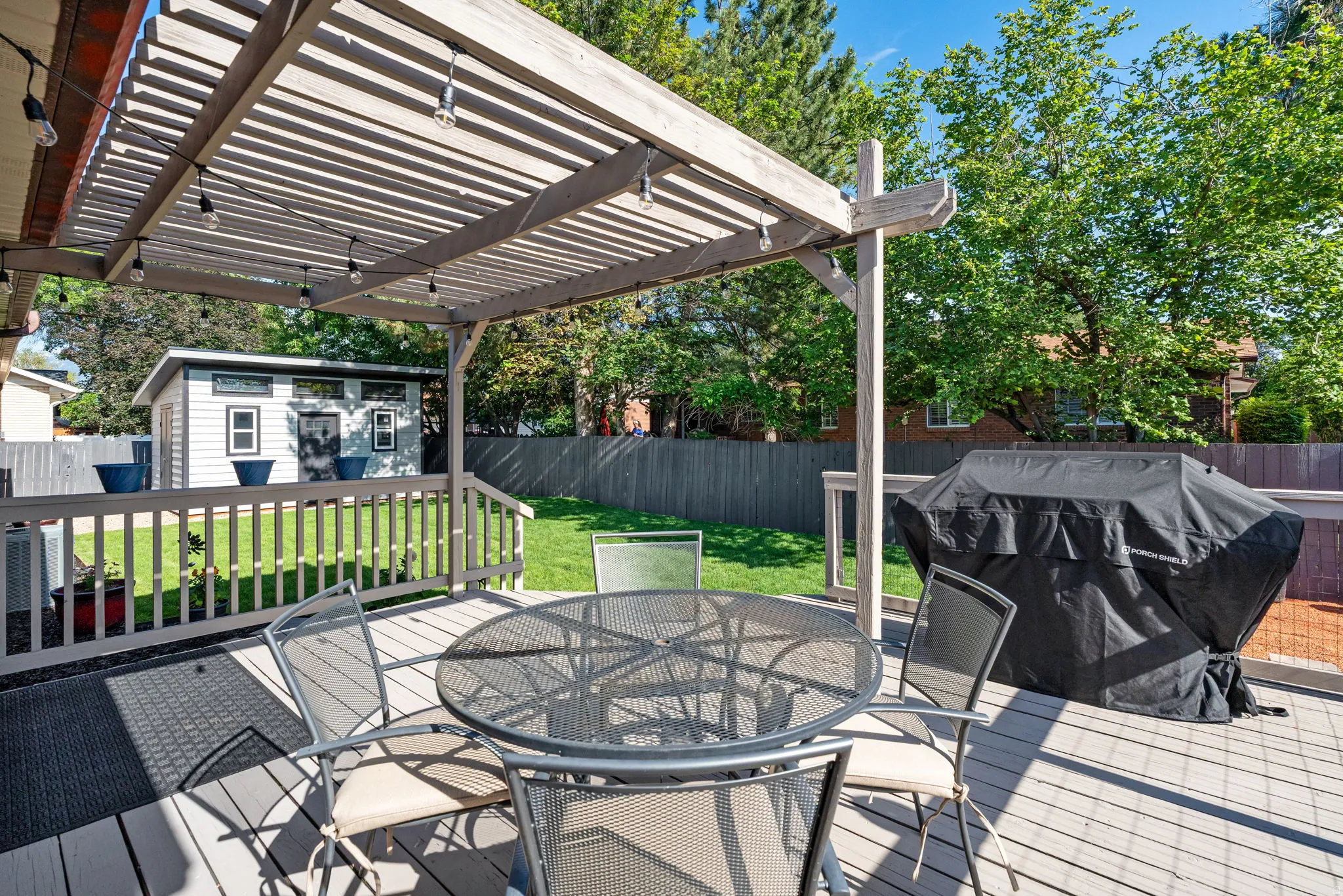 Expansive outdoor deck featuring a wooden pergola, string lighting, and a slatted railing