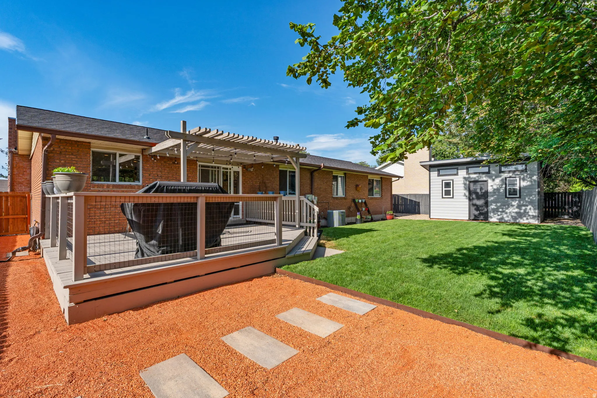 Expansive backyard featuring a large composite deck with a pergola, a manicured lawn, a modern shed, and a stone paver pathway