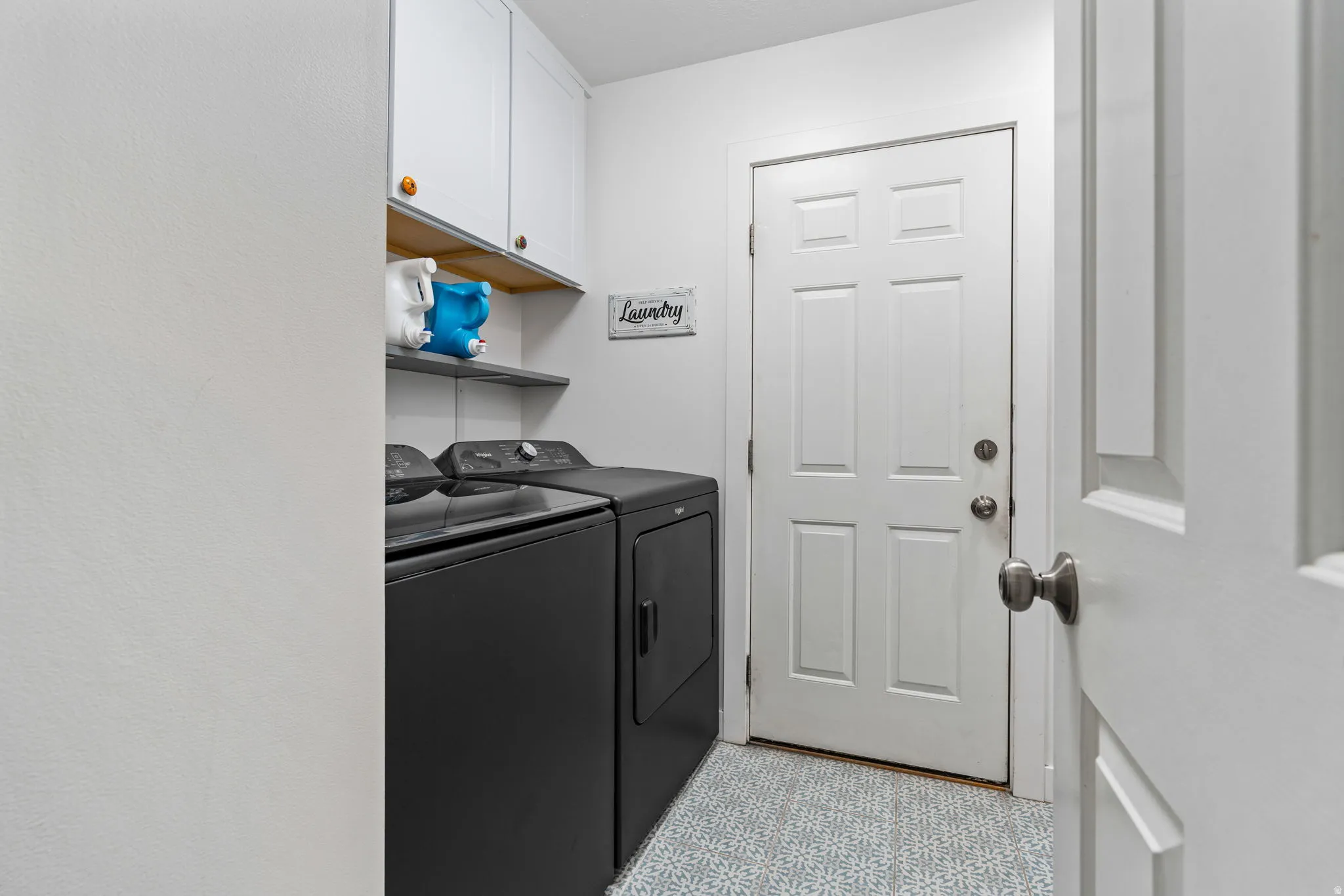 Dedicated laundry area featuring white shaker cabinetry with wood-finish accents, open shelving, and a six-panel interior door