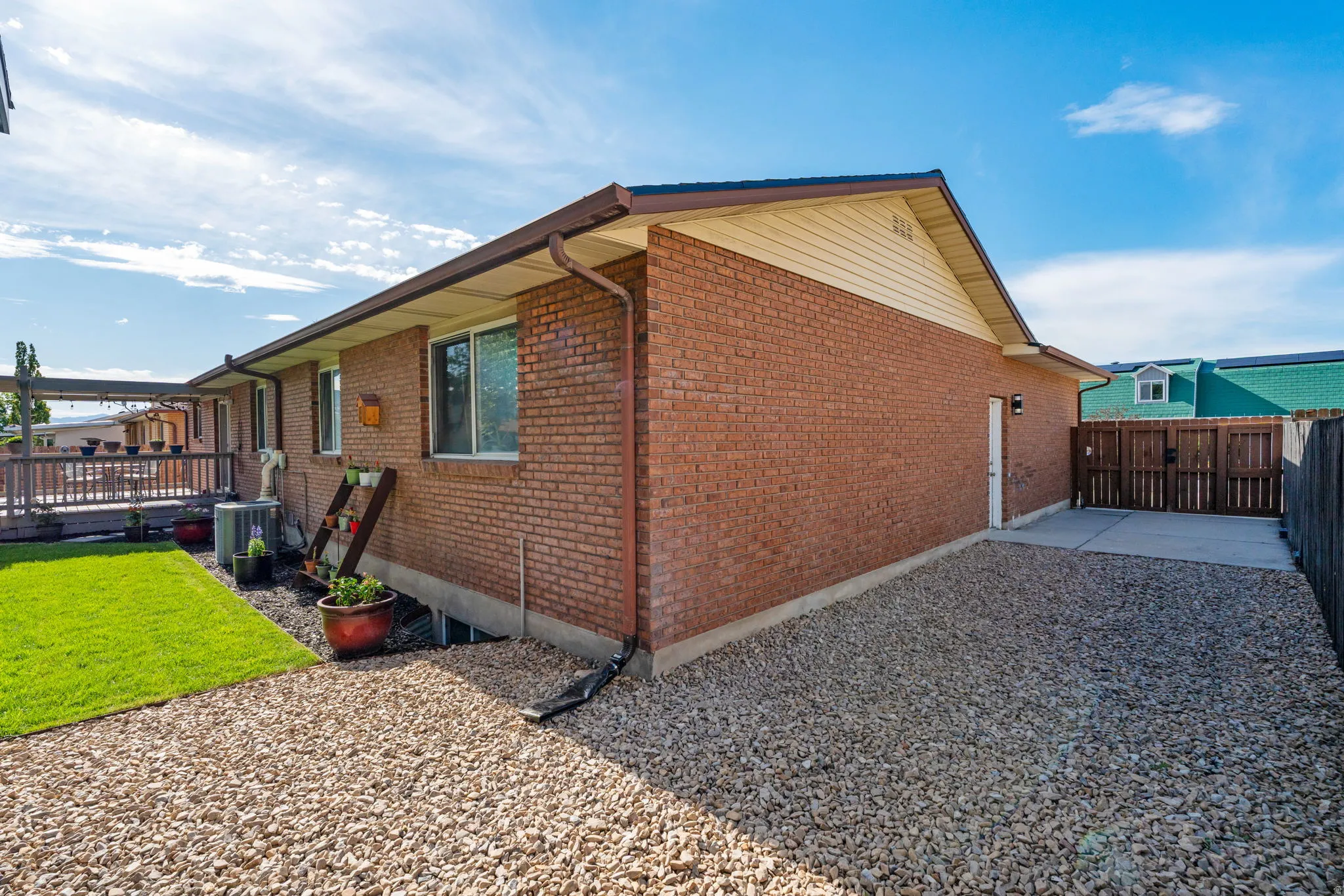 Brick exterior featuring a wood deck, a manicured lawn, a gravel patio area, a concrete pad, and a privacy fence