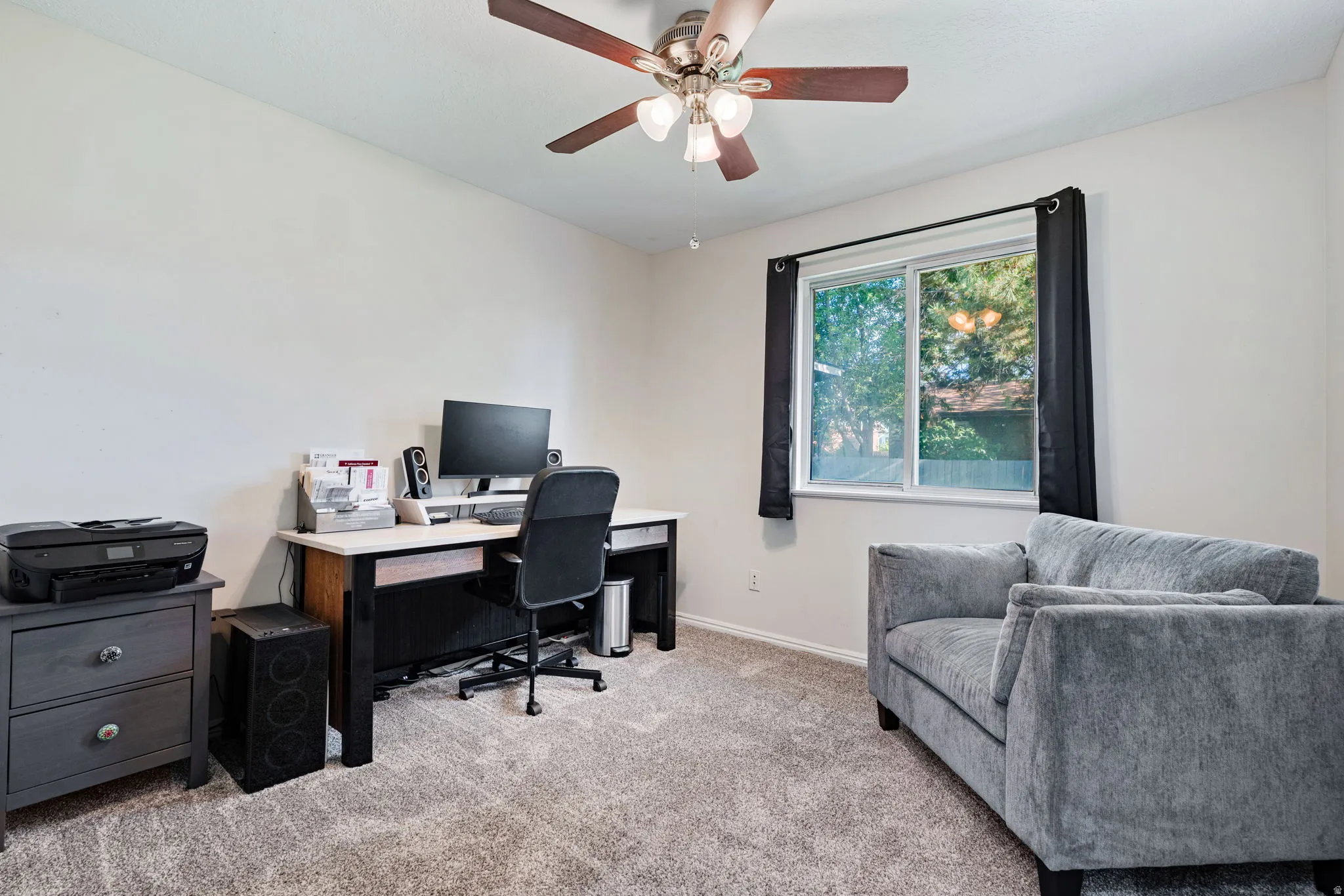 Carpeted room with a ceiling fan light fixture, a window with dark drapery, and neutral wall tones