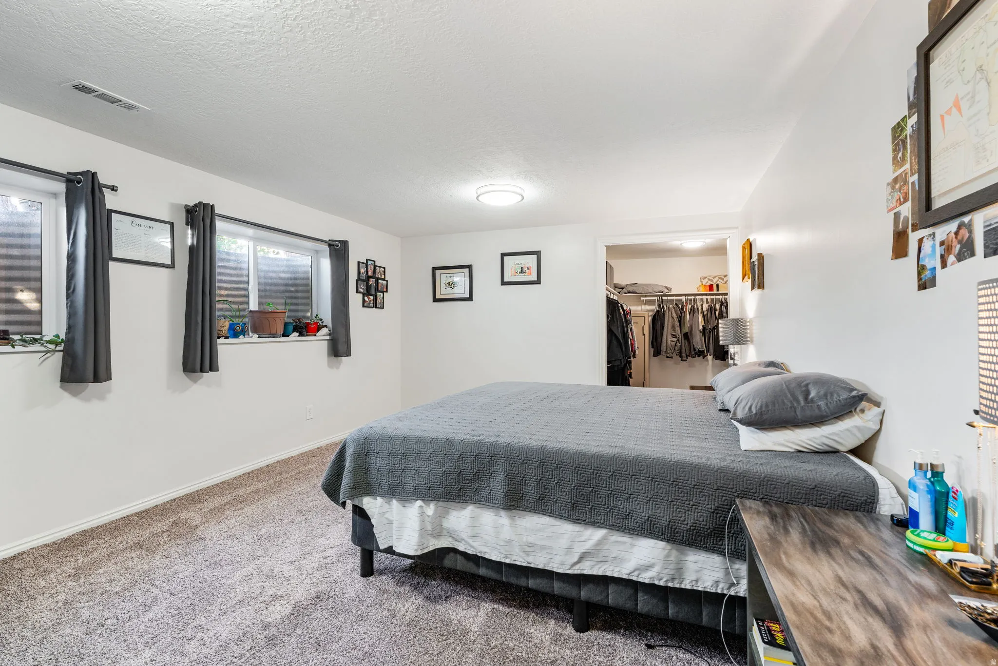 Spacious room featuring neutral carpeting, white walls, multiple windows, a ceiling-mounted light fixture, and an open closet with shelving and hanging rods