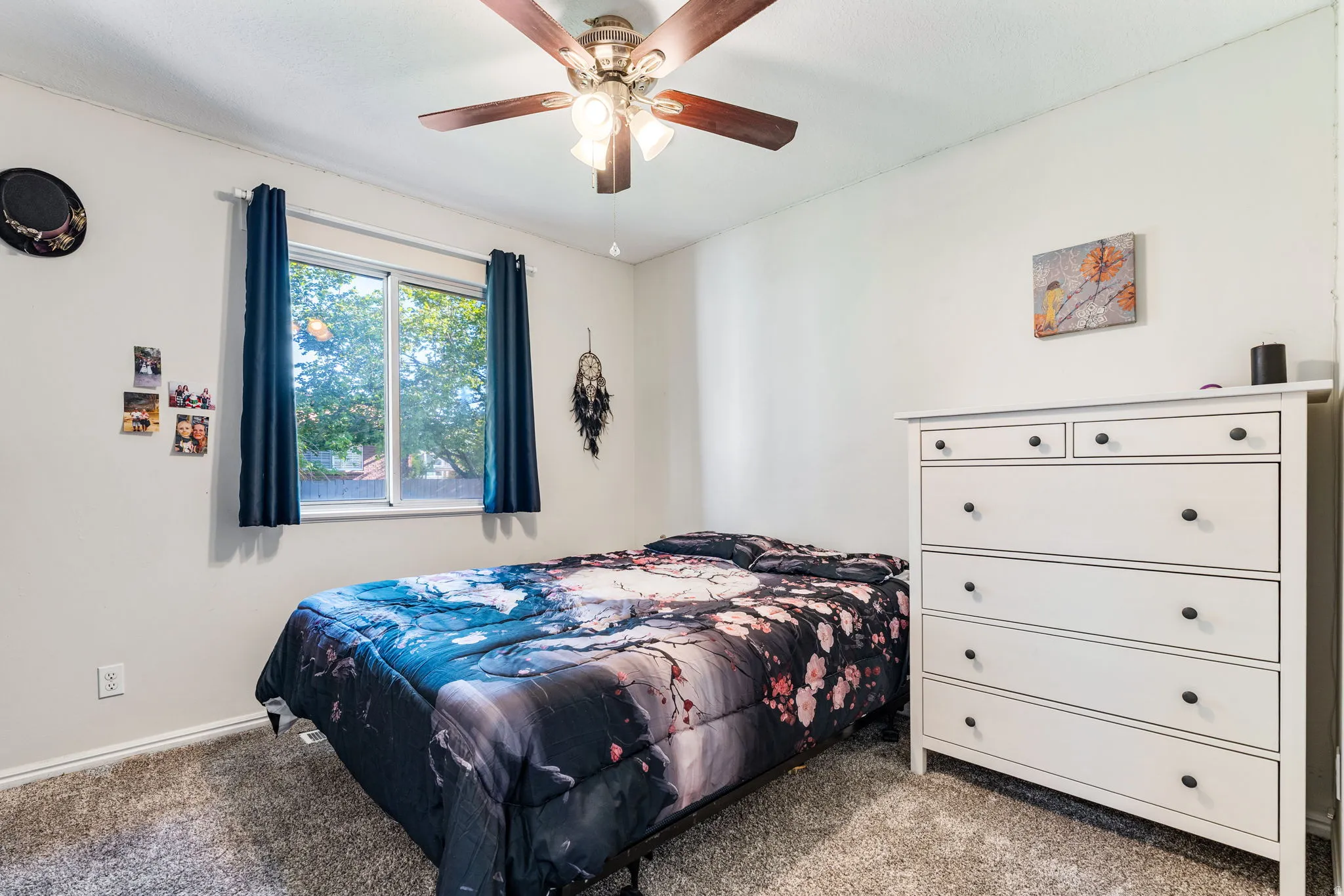 Bedroom featuring plush carpeting, a multi-speed ceiling fan with integrated lighting, and a window with a green outdoor backdrop