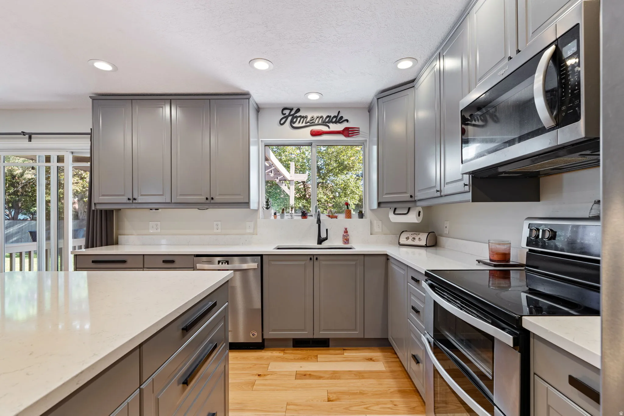 Modern kitchen featuring light gray cabinetry, stainless steel appliances, light countertops, wood-finish flooring, and recessed lighting