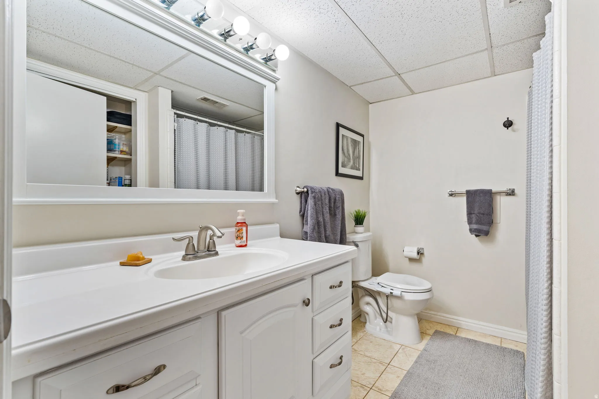 Bathroom featuring a single vanity with a white countertop and base cabinetry, brushed nickel faucet, large wall mirror, and overhead vanity lighting