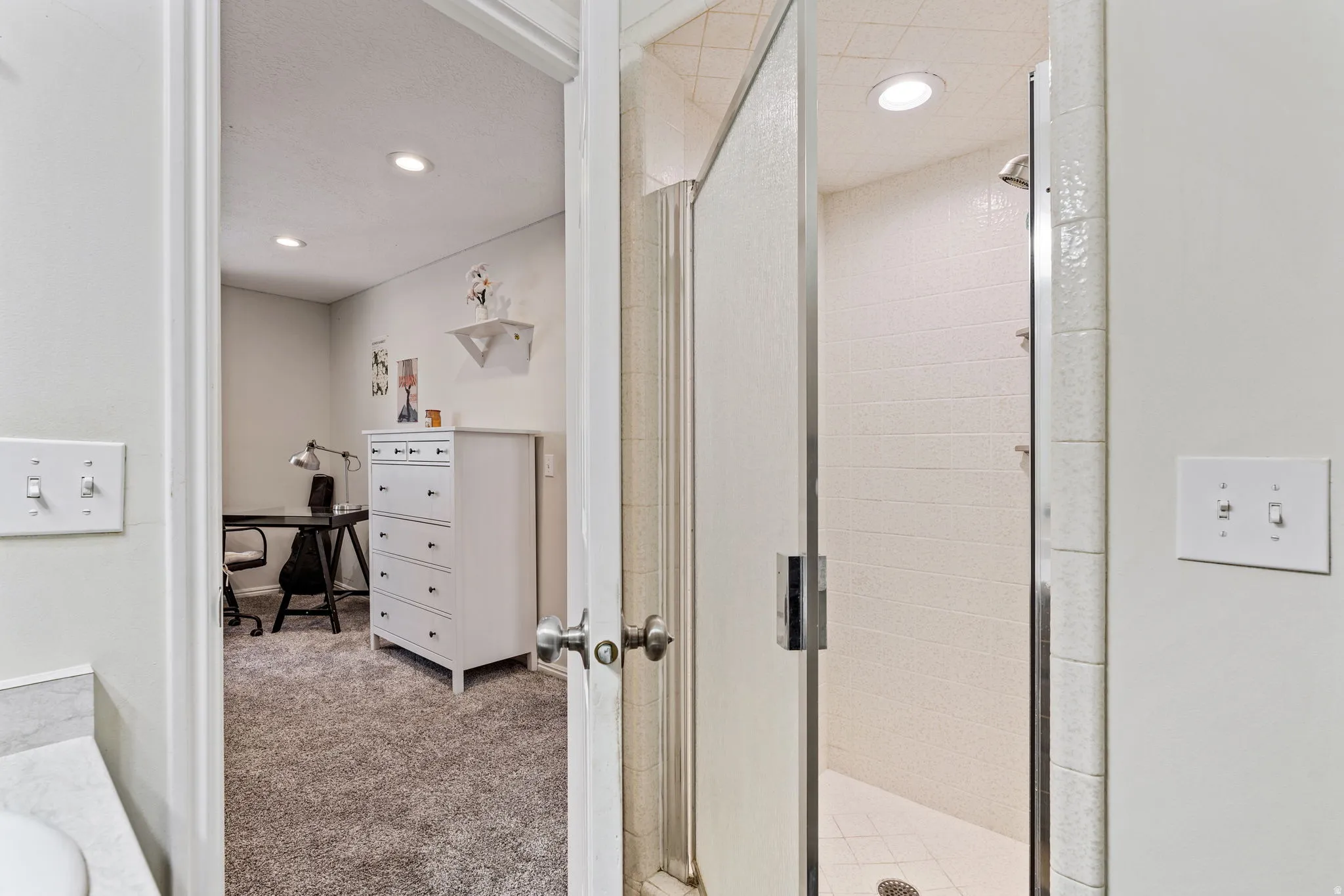 Glass-enclosed shower with white tiled walls and recessed lighting
