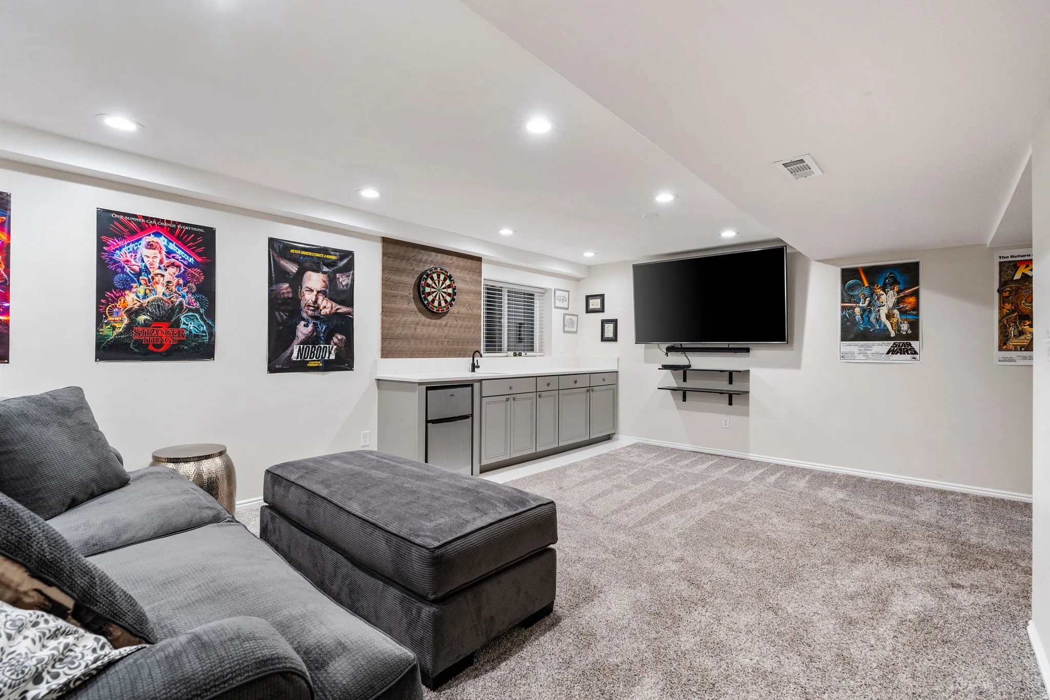 Lower-level entertainment space featuring recessed lighting, a built-in wet bar with gray cabinetry, a beverage refrigerator, and a dark stone-finish countertop