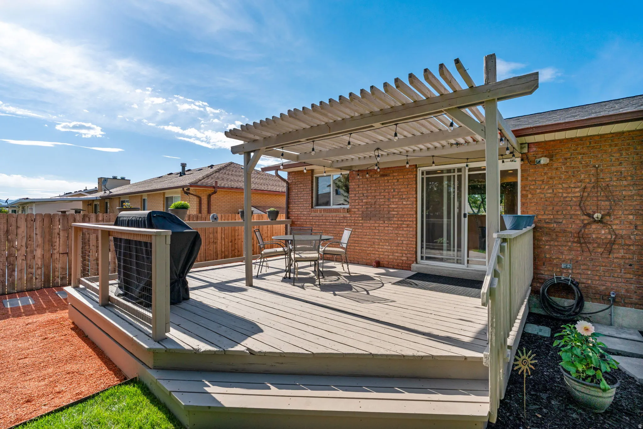 Spacious outdoor deck featuring a slat pergola with string lighting, direct access through sliding glass doors, a privacy fence, and a brick exterior