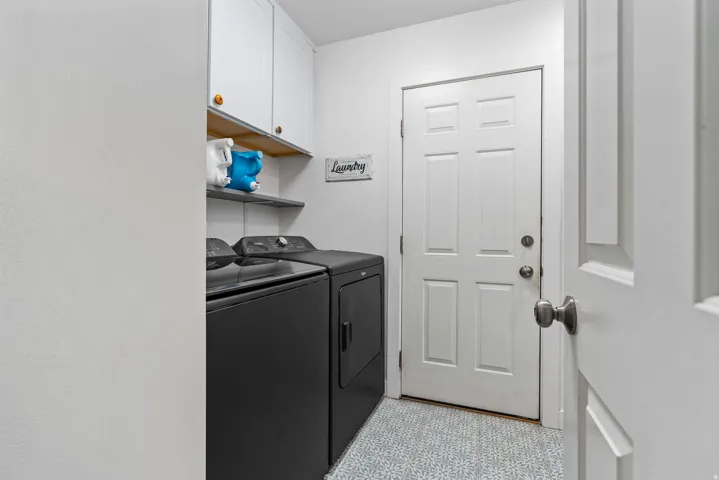 Dedicated laundry area featuring white shaker cabinetry with wood-finish accents, open shelving, and a six-panel interior door