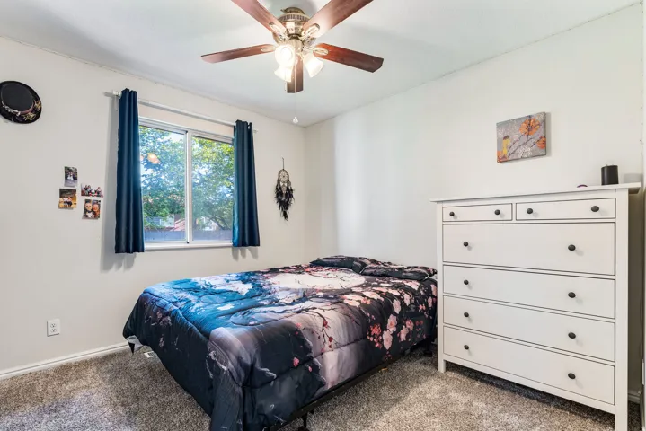 Bedroom featuring plush carpeting, a multi-speed ceiling fan with integrated lighting, and a window with a green outdoor backdrop