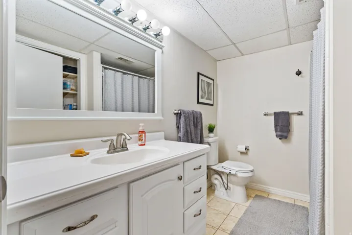 Bathroom featuring a single vanity with a white countertop and base cabinetry, brushed nickel faucet, large wall mirror, and overhead vanity lighting