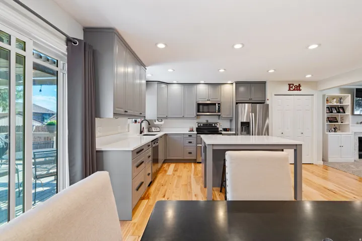 Well-appointed kitchen featuring light gray cabinetry, white countertops, stainless steel appliances, a center island with seating, and wood-finish flooring