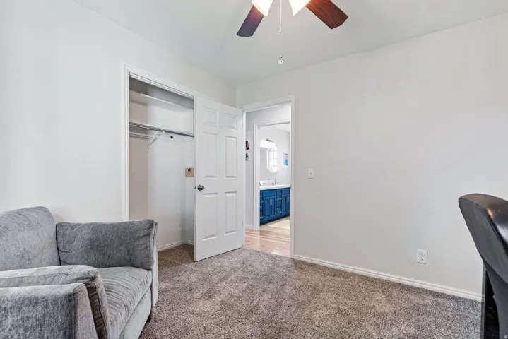 Carpeted room with white walls, a ceiling fan, and a built-in closet with sliding doors