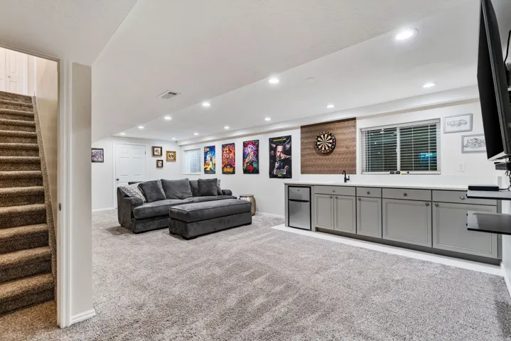 Finished lower level featuring recessed lighting, a built-in wet bar with a mini-fridge, a window with horizontal blinds, and a wood-finish accent wall