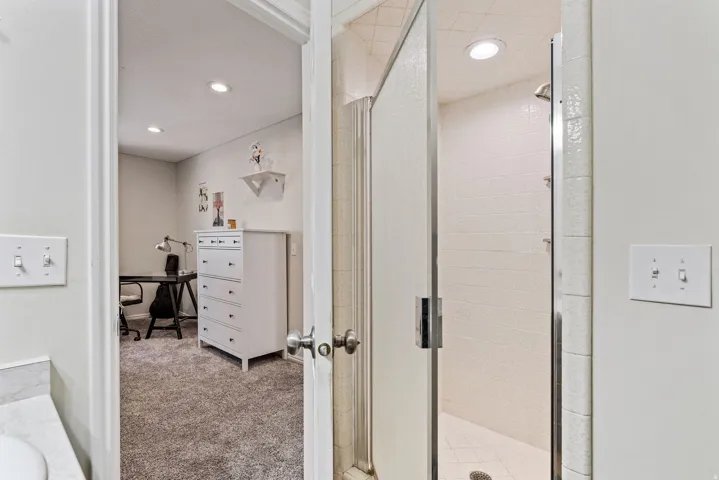 Glass-enclosed shower with white tiled walls and recessed lighting