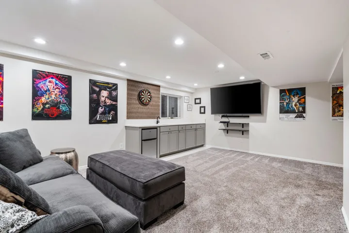 Lower-level entertainment space featuring recessed lighting, a built-in wet bar with gray cabinetry, a beverage refrigerator, and a dark stone-finish countertop
