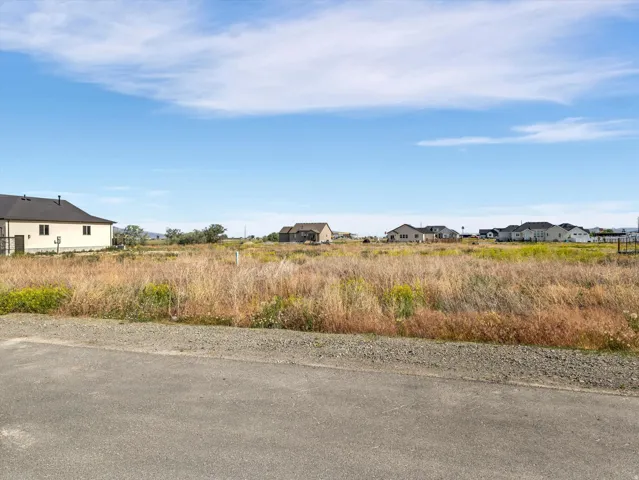 Expansive land parcel featuring natural grasses and distant residential structures