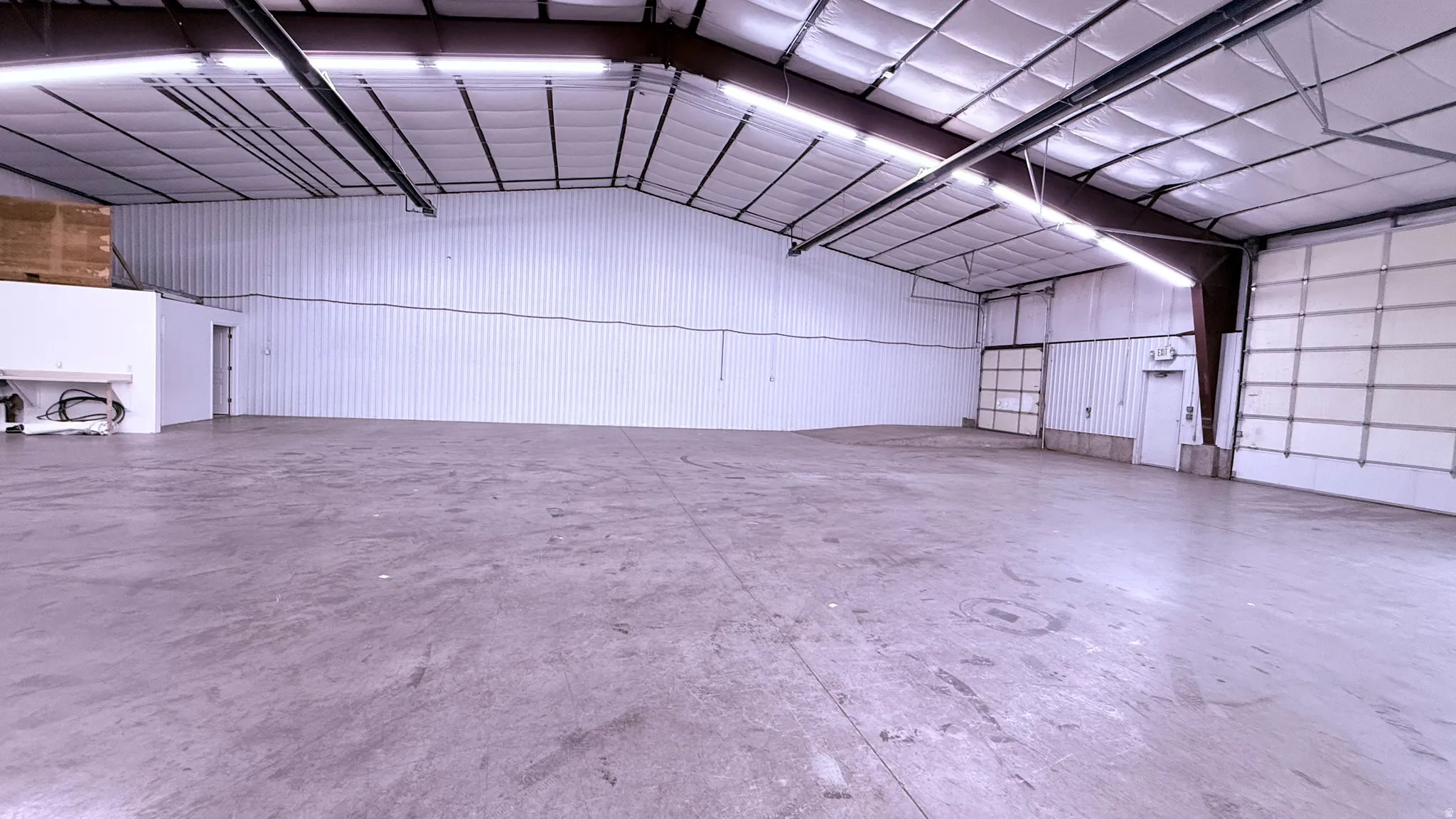 Spacious concrete flooring, corrugated metal walls, exposed structural beams, high ceilings, and multiple overhead doors
