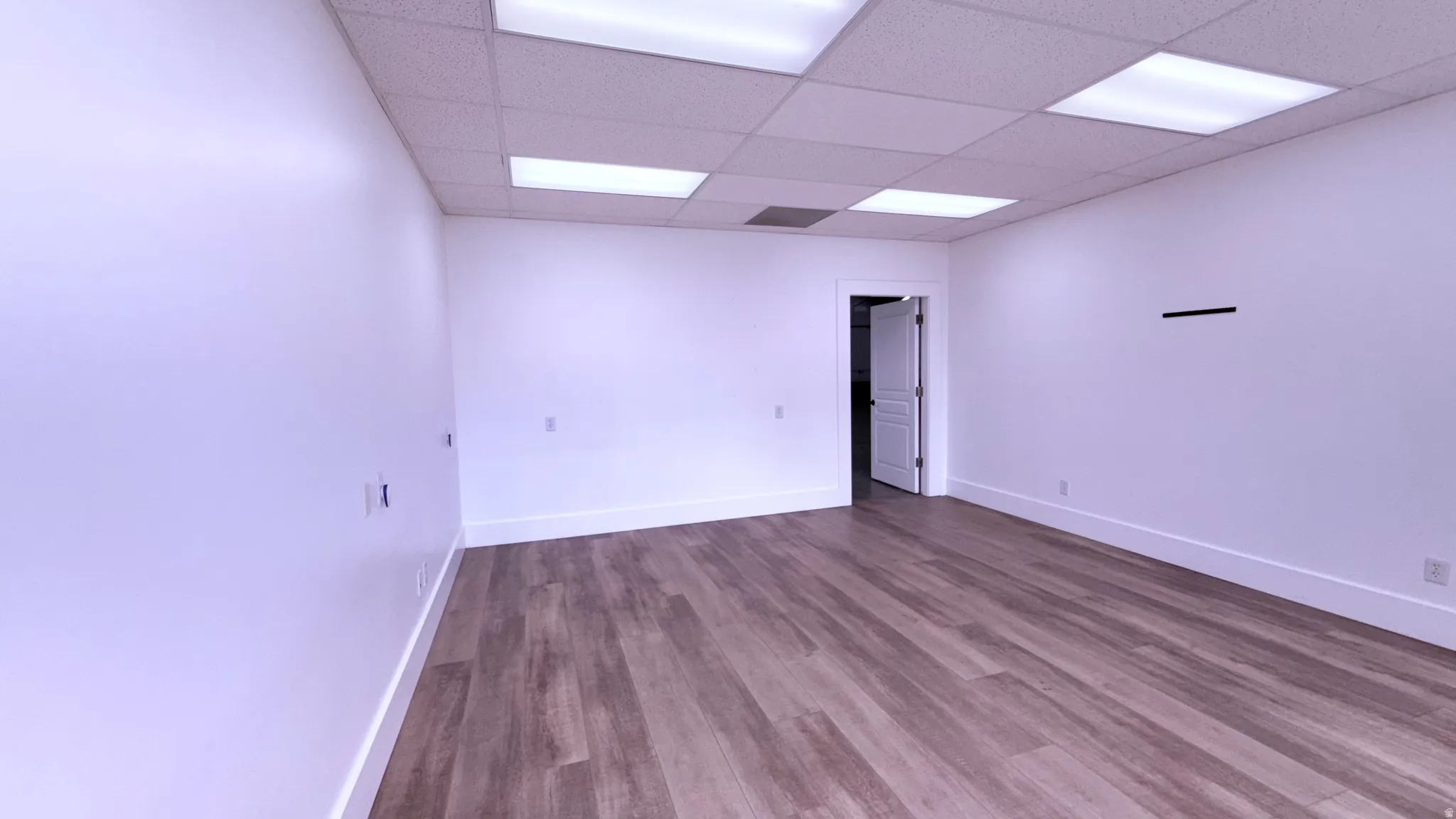 Wood-finish flooring, white walls, drop ceiling with integrated lighting, and a white interior door