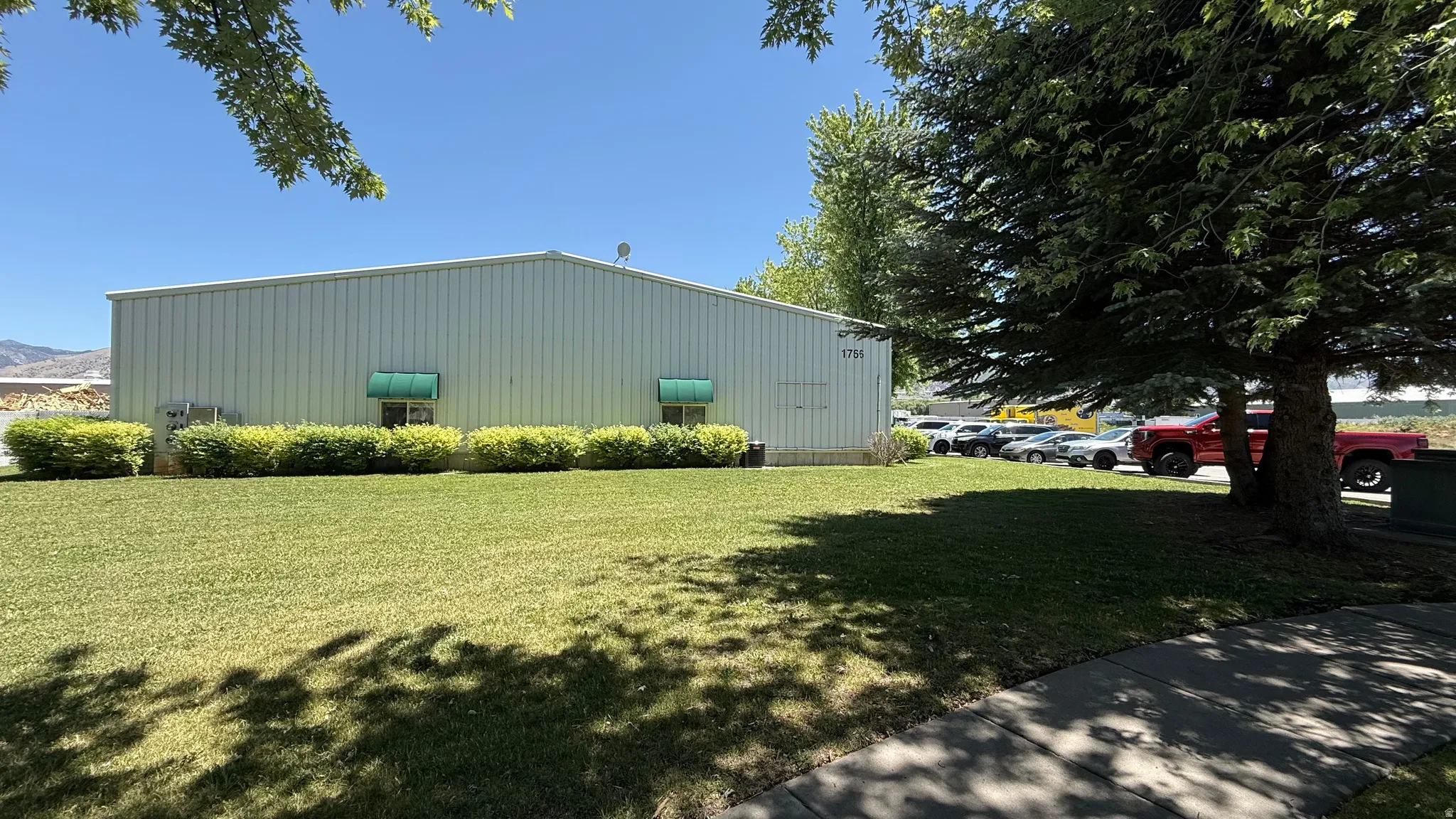 Commercial building with corrugated metal siding, featuring a substantial front lawn and mature trees