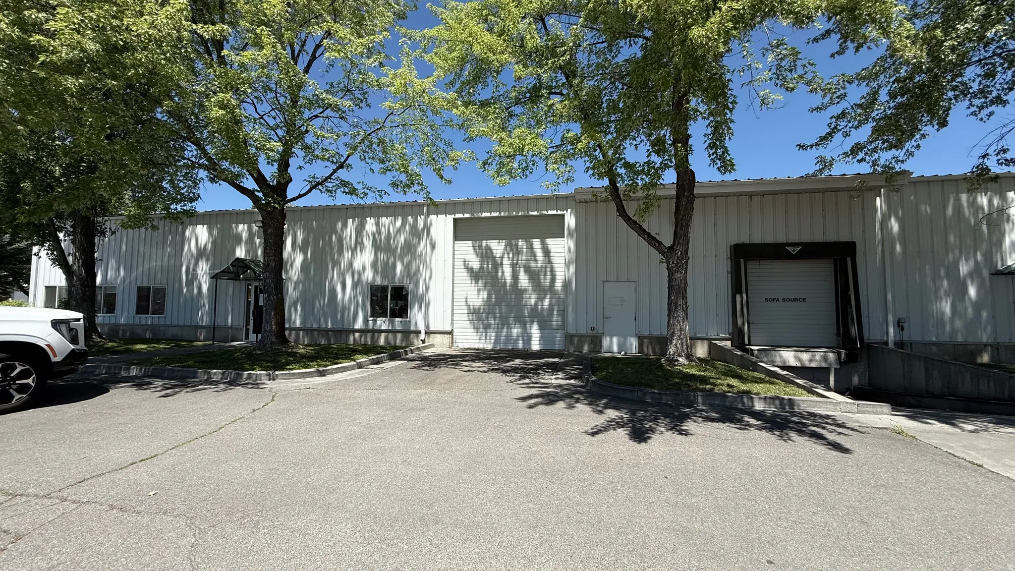 Industrial building featuring a corrugated metal exterior, multiple roll-up doors, a covered entry, and paved access