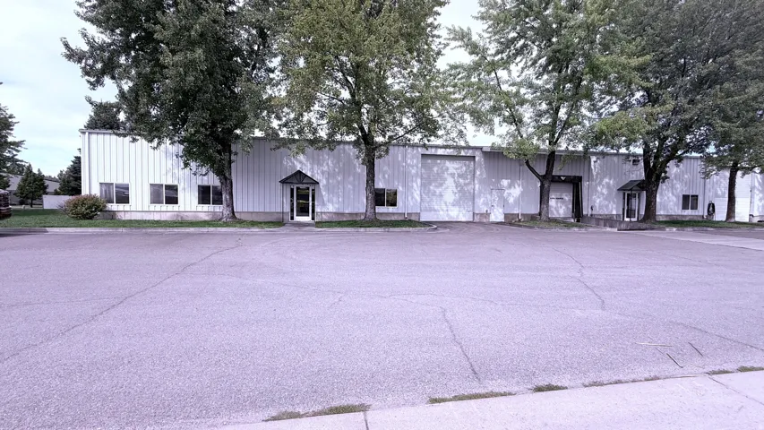 Expansive parking lot fronting a commercial building with multiple entry points, large roll-up doors, and prominent window sections