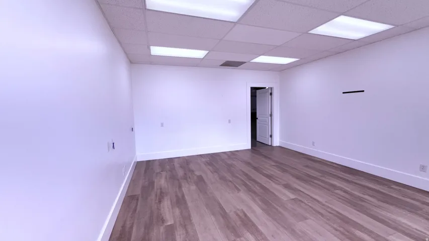 Wood-finish flooring, white walls, drop ceiling with integrated lighting, and a white interior door