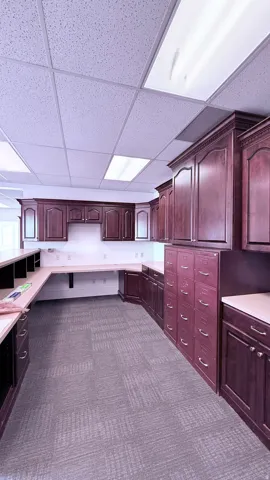 Integrated dark wood-finish cabinetry, extensive built-in workspace, patterned carpet, and drop ceiling with recessed lighting