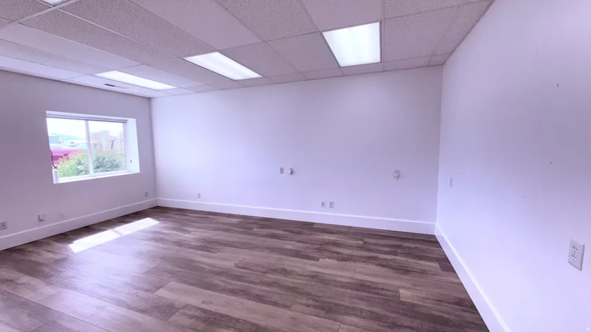 Spacious interior with wood-finish flooring, white painted walls, and a drop ceiling with integrated rectangular lighting fixtures