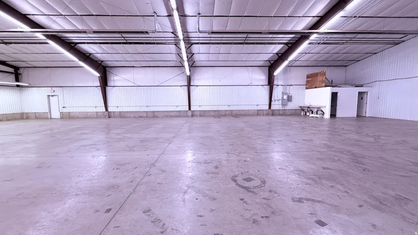 Expansive open floor plan with concrete flooring, high ceilings with exposed metal beams, and fluorescent lighting