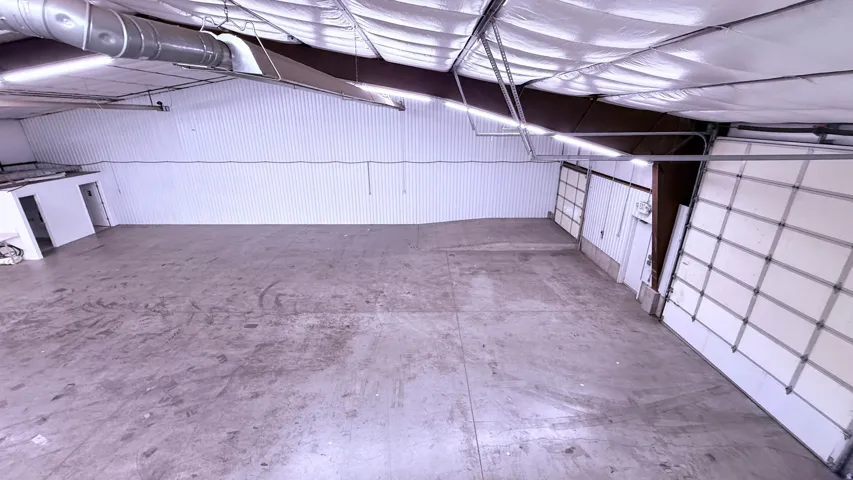 Expansive open-concept space featuring concrete flooring, multiple roll-up doors, high ceilings with exposed ductwork, and abundant overhead lighting