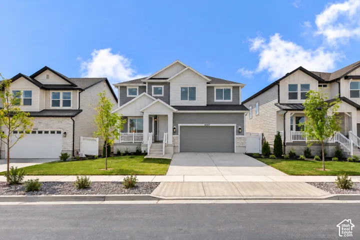 Modern two-story residence featuring a gray and white facade, an attached two-car garage, a covered front porch, and mature landscaping
