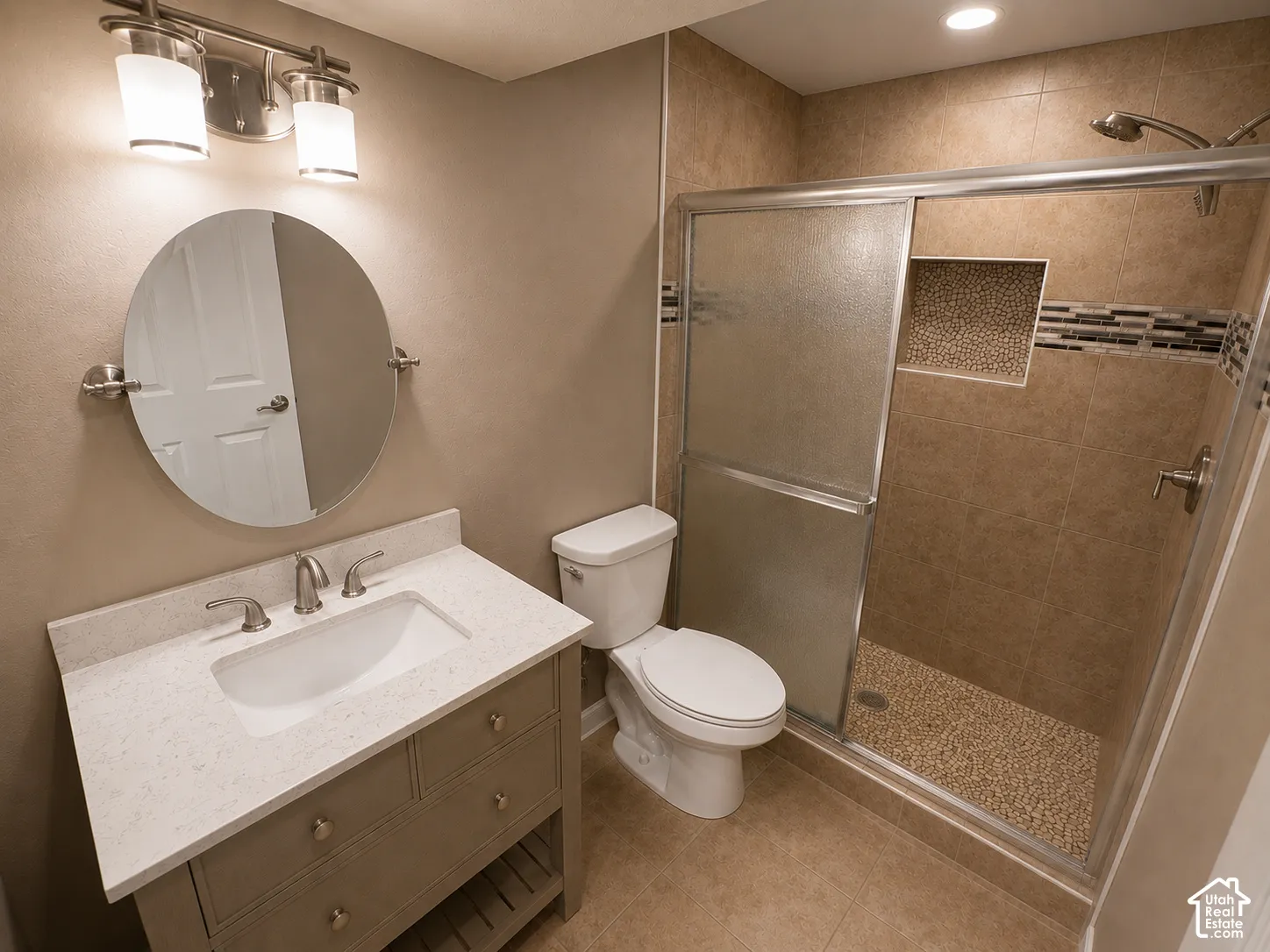 Bathroom featuring a single vanity with stone-finish countertop, brushed nickel faucet, and a circular mirror