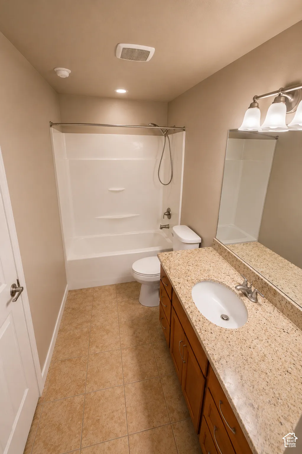 Bathroom featuring a wood-finish vanity with a light speckled countertop, an undermount sink, and a mirrored wall