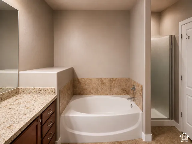 Bathroom featuring a soaking tub with tile surround, a separate shower with a frosted glass enclosure, and a vanity with a granite-style countertop and wood cabinetry