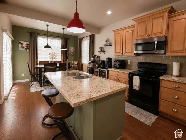 Kitchen featuring a central island with a double sink, stone-finish countertops, wood-finish flooring, light wood cabinetry, and a subway tile backsplash