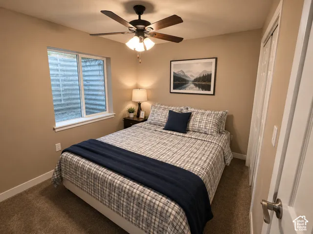Carpeted room featuring a ceiling fan, a window with a white frame, and a closet with bifold doors