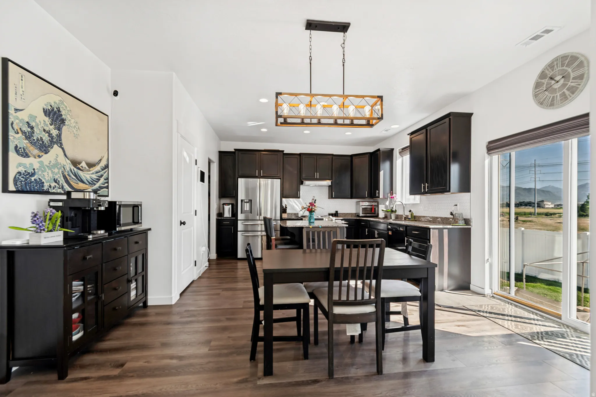 Open-concept kitchen and dining area featuring rich wood-finish flooring, dark cabinetry, and a subway tile backsplash