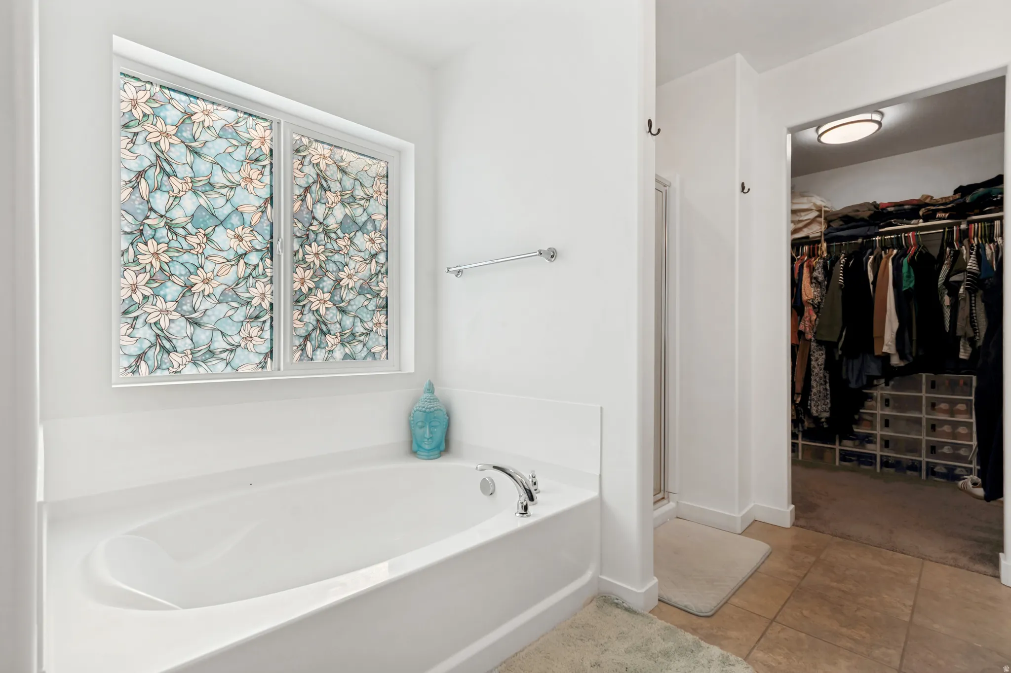 Soaking tub with a patterned privacy window, complemented by light-toned wall paint and an adjacent walk-in closet with built-in shelving