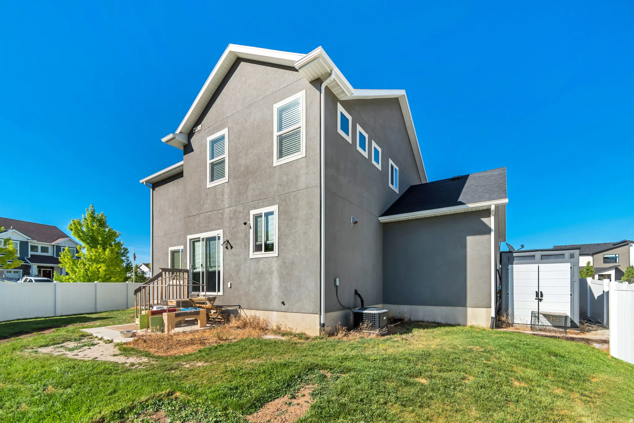 Rear exterior featuring a sliding glass door, multiple windows, a white vinyl fence, an outdoor shed, and a concrete patio