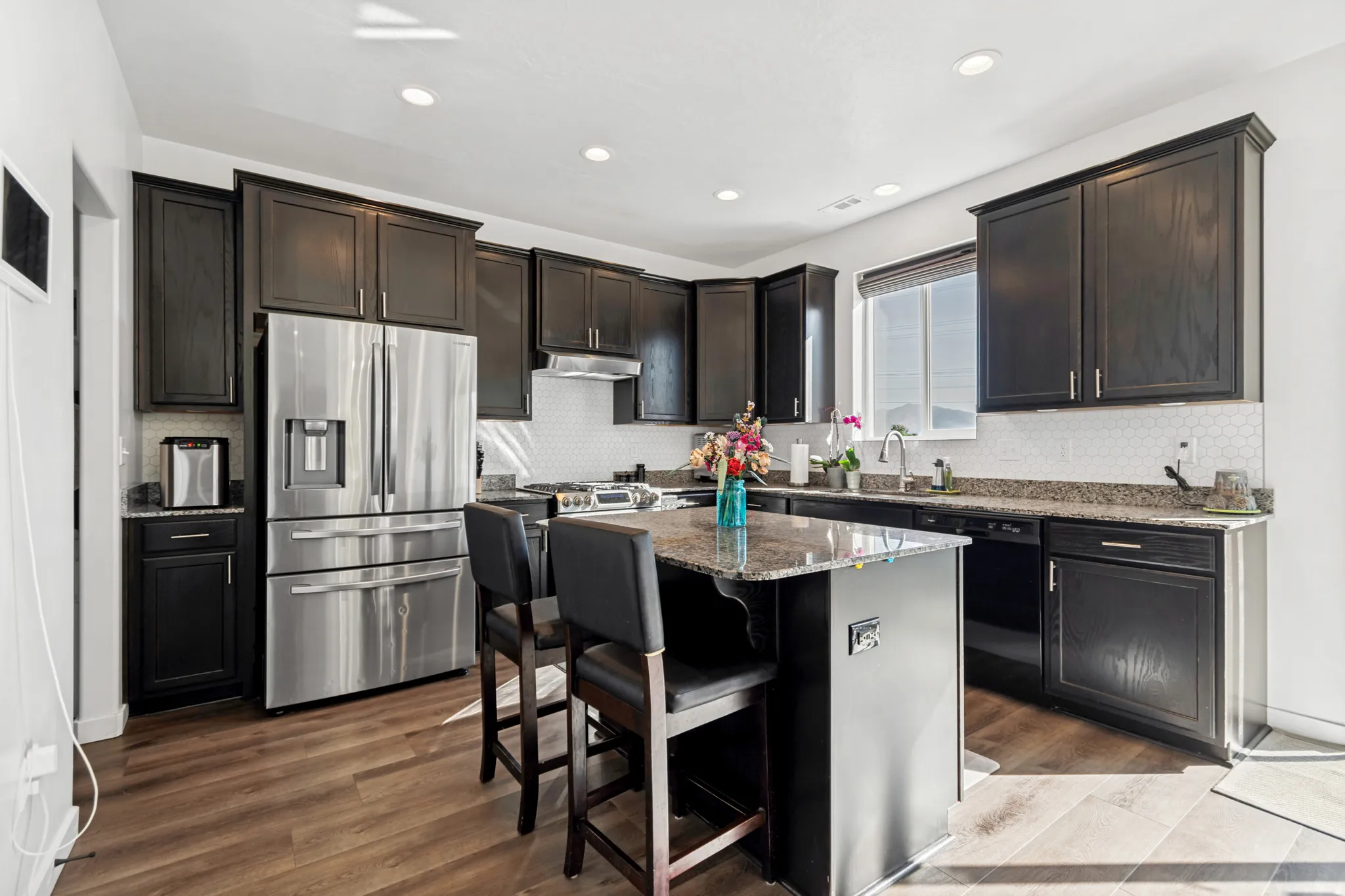 Modern kitchen featuring dark wood cabinetry, a stainless steel French-door refrigerator, granite countertops, and a white hexagonal tile backsplash
