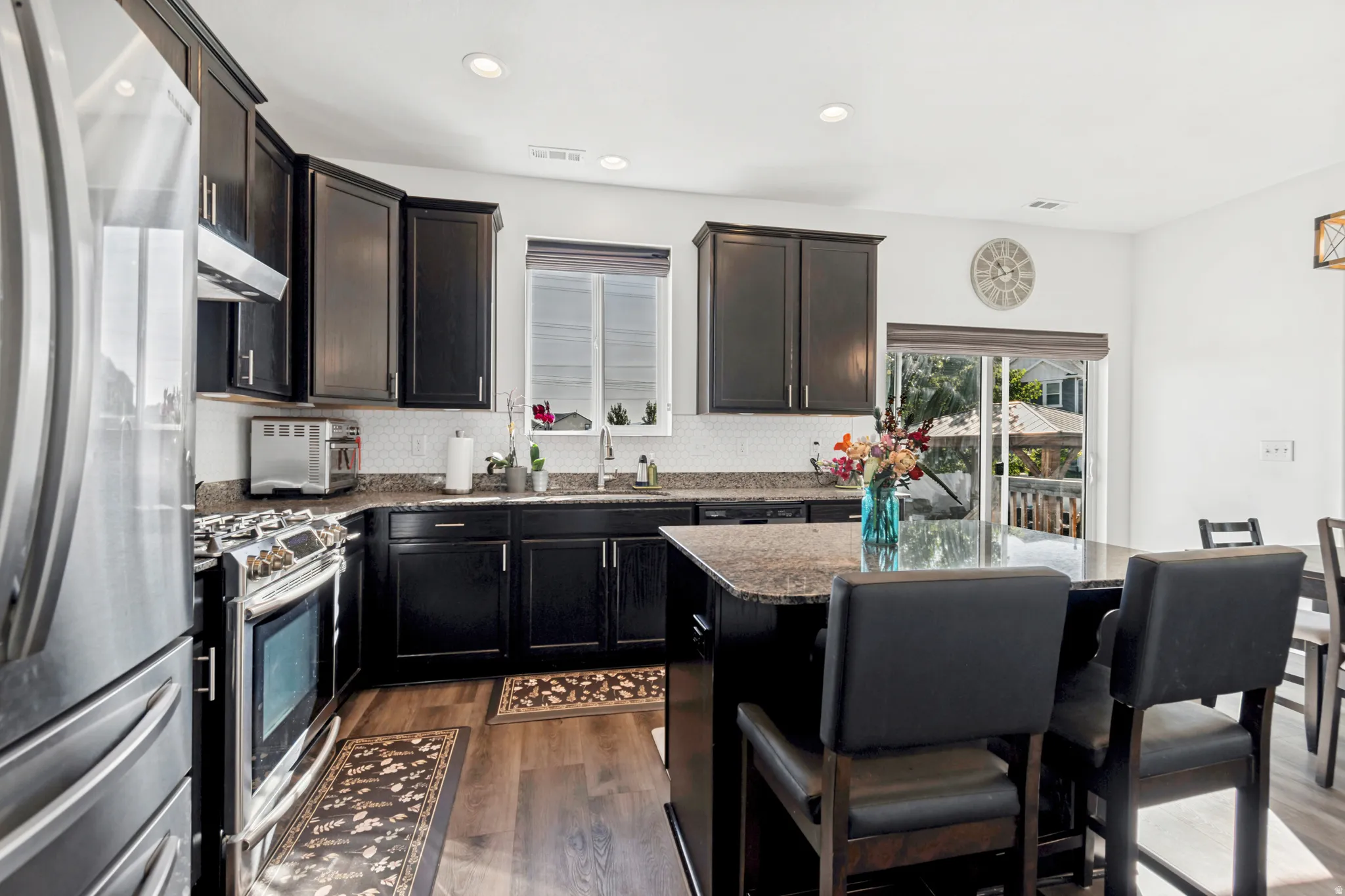 Modern kitchen featuring dark cabinetry, stainless steel appliances, and wood-finish flooring