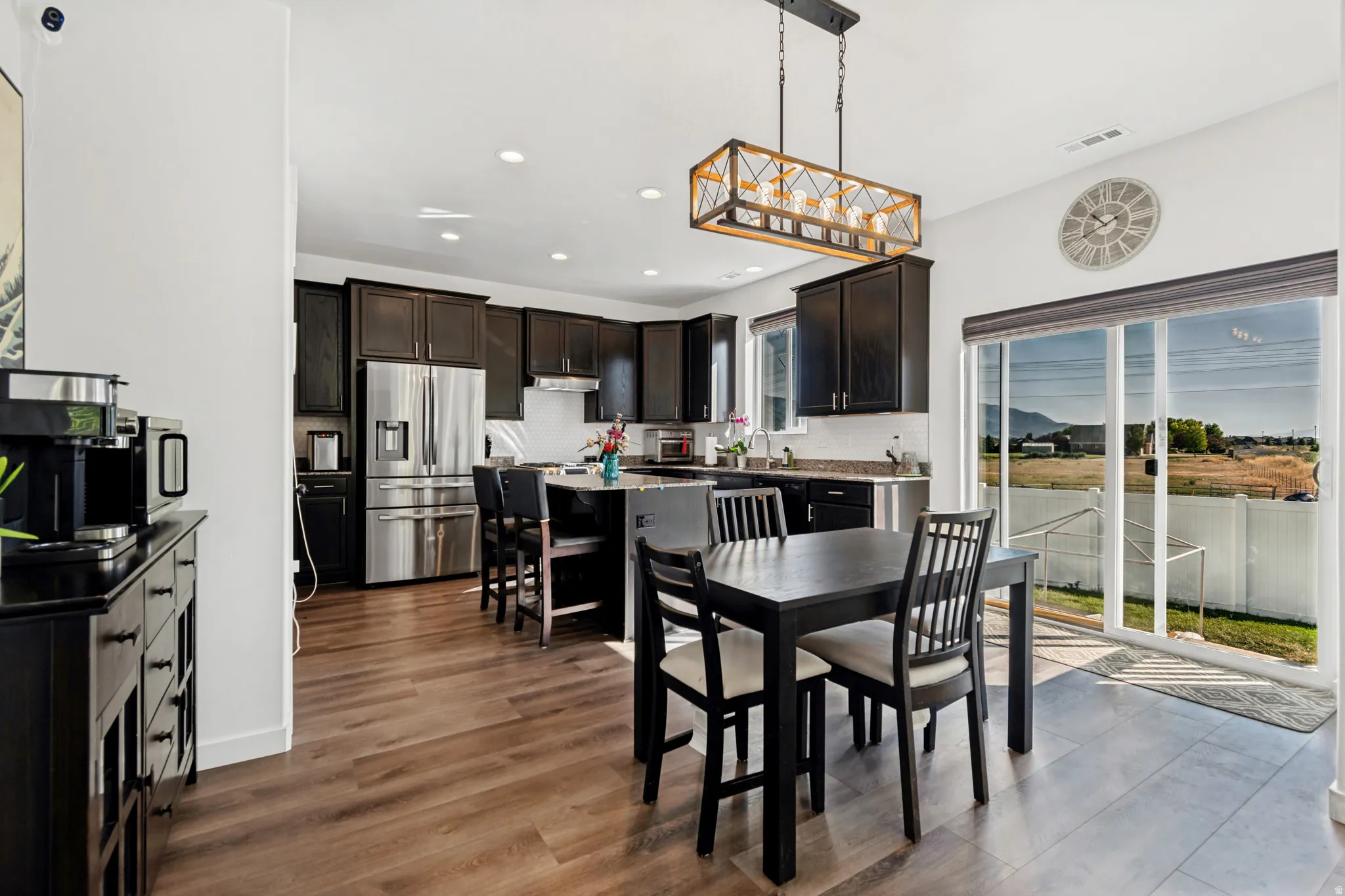 Open-concept kitchen and dining area featuring dark wood-finish cabinetry, stainless steel appliances, a center island with bar seating, wood-finish flooring, and a sliding glass door providing outdoor access