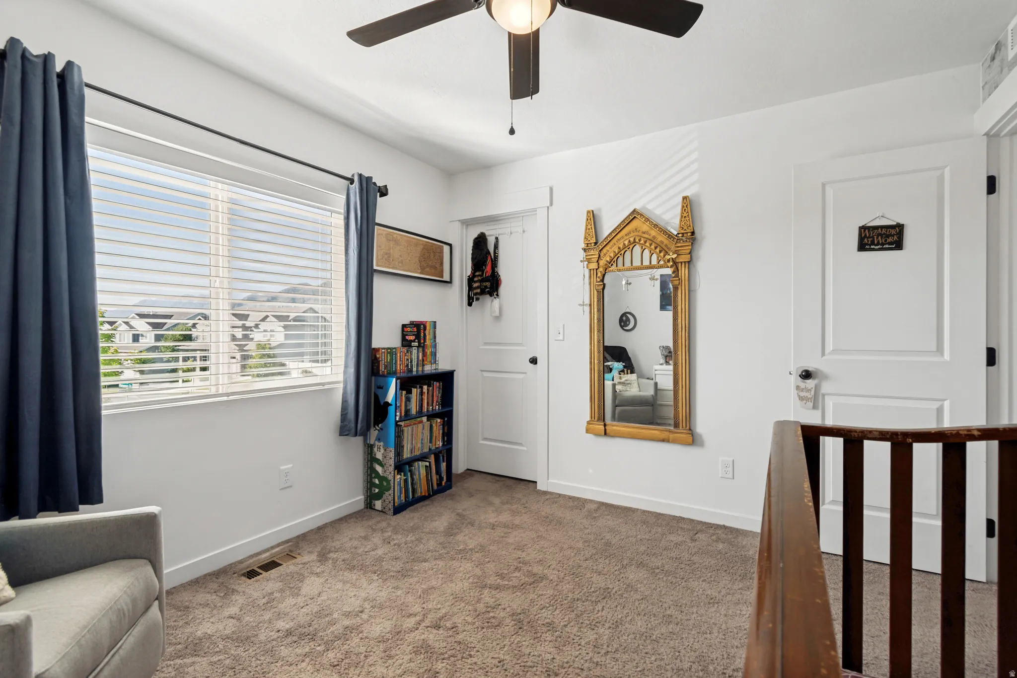 Carpeted room with a ceiling fan, a large window featuring blinds, and a built-in bookshelf