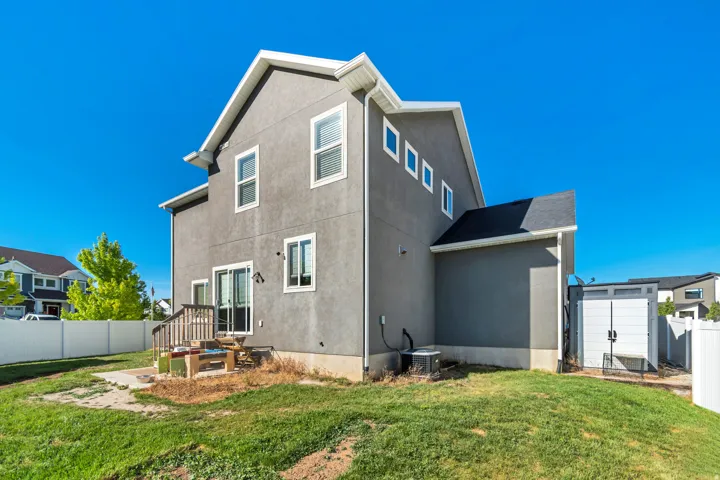 Rear exterior featuring a sliding glass door, multiple windows, a white vinyl fence, an outdoor shed, and a concrete patio