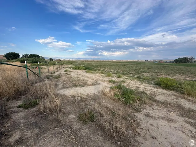 Expansive open land featuring diverse terrain, distant structures, and a clear horizon under a broad sky