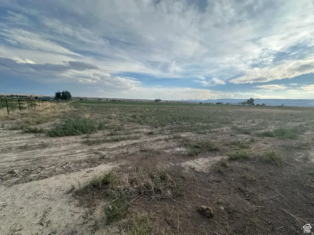 Expansive open land featuring a dirt path, partial fencing, and distant structures under a broad sky